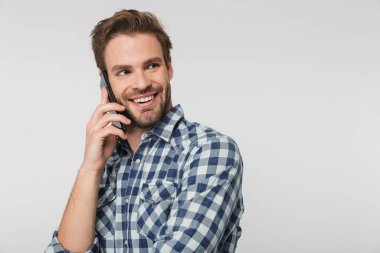 Ekose gömlek giyen neşeli bir gencin portresi. Beyaz arka planda izole edilmiş, gülümseyen ve cep telefonuyla konuşan.