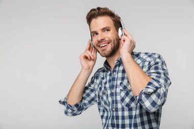 Ekose gömlek giyen, kulaklık takan ve beyaz arka planda izole bir şekilde gülümseyen genç adamın portresi.
