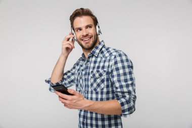 Beyaz arka planda izole edilmiş cep telefonuyla kulaklık takan gülümseyen genç adamın portresi.