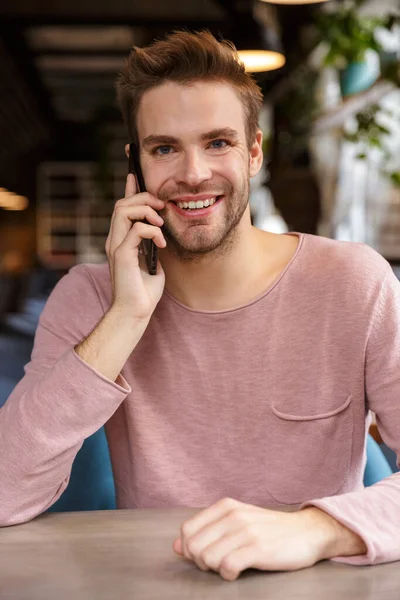 Привлекательный Улыбающийся Молодой Человек Разговаривает Мобильному Телефону Сидя Столом Кафе — стоковое фото