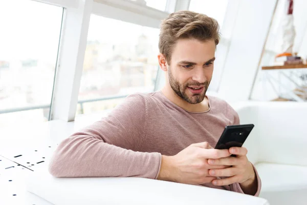 Obrázek Mladého Vousatého Muže Pomocí Smartphonu Při Sezení Pohovce Okna — Stock fotografie