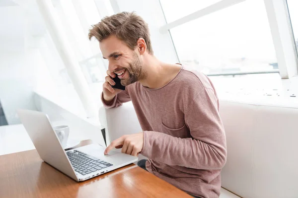 Imagem Jovem Barbudo Usando Smartphone Laptop Enquanto Sentado Sofá Pela — Fotografia de Stock