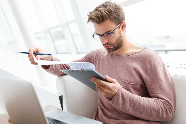 Imagen Joven Barbudo Usando Portátil Sujetando Portapapeles Mientras Trabajaba Café — Foto de Stock