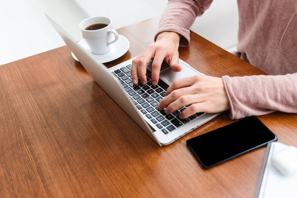 Изображение молодого кавказца, пьющего кофе и работающего за ноутбуком в кафе в помещении
