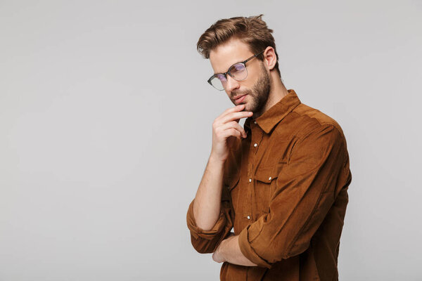 Portrait of unshaven young man wearing eyeglasses posing and looking at camera isolated over white background