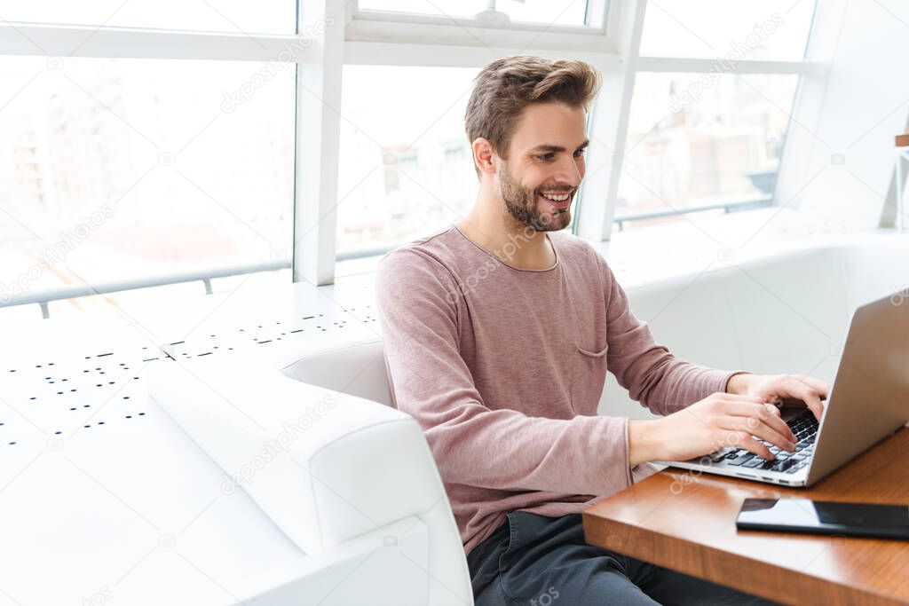 Image of young bearded man working on laptop computer while sitting in cafe indoors