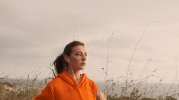 海岸で走っているイヤホンの深刻なかなり運動能力の女性 — ストック動画