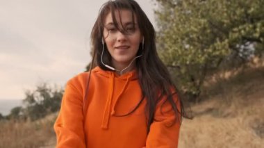 Neşeli, güzel, kulaklıklı atletik kadın deniz kıyısında yürüyor ve kameraya bakıyor.