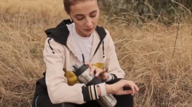 Kulaklıklı, yorgun ve atletik bir kadın. Eğitimden sonra deniz kıyısında kol saatini kullanırken dinleniyor.