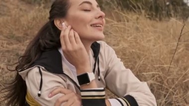 Kulaklıklı neşeli, güzel, atletik kadının yakın görüntüsü eğitimden sonra dinleniyor ve deniz kıyısında gözleri kapalı müzik dinliyor.
