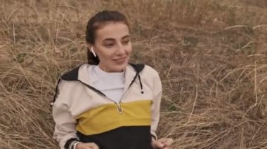 Kulaklıklar takmış, müzik dinleyen ve deniz kenarında otururken anın tadını çıkaran güzel, güzel atletik bir kadın.