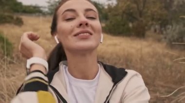 Kulaklıkla gülümseyen, güzel atletik bir kadın. Müzik dinliyor ve deniz kenarında otururken anın tadını çıkarıyor.