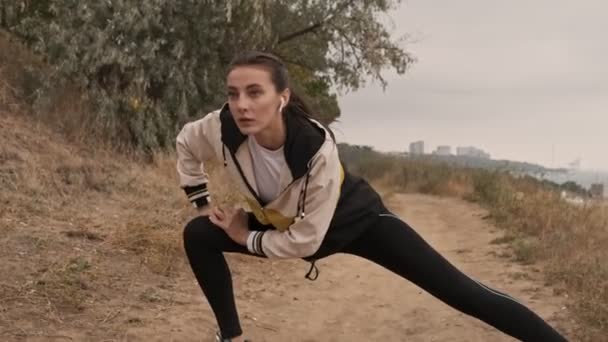 Kulaklıklı Deniz Kıyısında Bacaklarıyla Isınan Konsantre Güzel Atletik Bir Kadın — Stok video