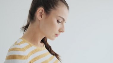 Düşünceli genç bir kadın, atölyedeki beyaz arka planda izole edilmiş akıllı telefonunu kullanıyor.