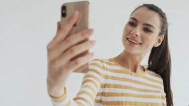 Pozitif genç bir kadın stüdyoda beyaz bir arkaplanda görüntülü görüşme yapıyor.