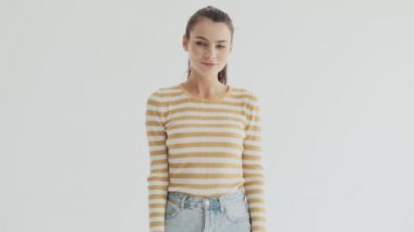 Kendine güvenen genç bir bayan stüdyoda beyaz bir arkaplanda iyi bir jest yapıyor.