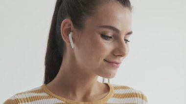 Oldukça hoş genç bir kadın, stüdyoda beyaz arka planda izole edilmiş kablosuz kulaklıklarını açıyor.