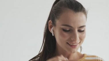Güzel genç bir kadın stüdyoda beyaz arka planda izole edilmiş kablosuz kulaklıklarını kullanarak müzik dinliyor.
