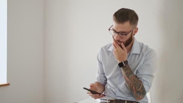 Egy Fókuszált Szemüveges Fiatal Munkás Használja Okostelefonját Miközben Fehér Irodában — Stock videók