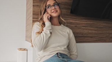 Güzel bir gülüşü olan genç bir bayan sabah mutfakta telefonla konuşuyor.