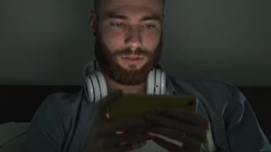 Geceleri gülümseyen genç bir adam akıllı telefonunu yatay olarak kullanıyor.