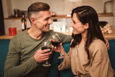 Evde mum ışığında romantik bir akşam yemeği yerken kırmızı şarap içen mutlu ve tutkulu çiftin görüntüsü.