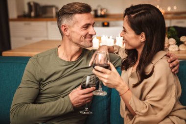 Evde mum ışığında romantik bir akşam yemeği yerken kırmızı şarap içen mutlu ve tutkulu çiftin görüntüsü.