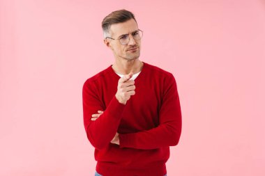 Gözlüklü yakışıklı beyaz adamın portresi pembe arka planda izole edilmiş kamerayı işaret ediyor.