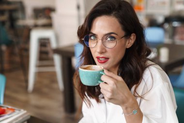 Kafe masasında otururken kahve içen çekici, genç bir esmer kadının fotoğrafını çek.