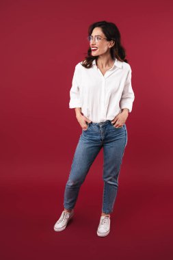 Kırmızı duvar arkasında yalnız poz veren mutlu ve pozitif gülümseyen genç bir kadının fotoğrafı..