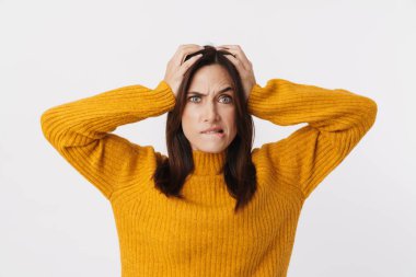 Stresli, esmer, süveter giyen, kaşlarını çatan ve beyaz arka planda rahatsız edici bir şekilde başını kavrayan bir kadın resmi.