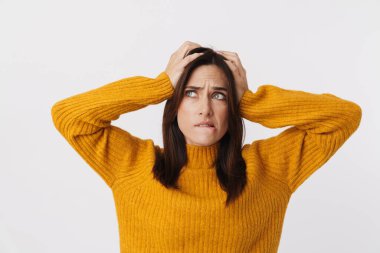 Stresli, esmer, süveter giyen, kaşlarını çatan ve beyaz arka planda rahatsız edici bir şekilde başını kavrayan bir kadın resmi.