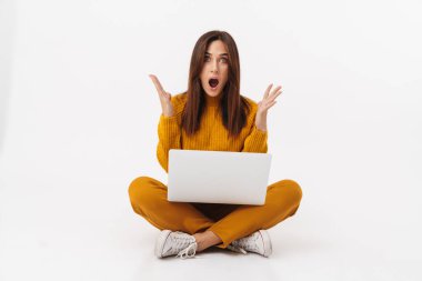 Image of beautiful brunette adult woman screaming and holding laptop computer while sitting with legs crossed isolated over white background clipart