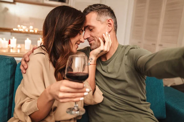 自宅でロマンチックなキャンドルライトディナーをしながら写真を撮る幸せな白人カップルのイメージ — ストック写真