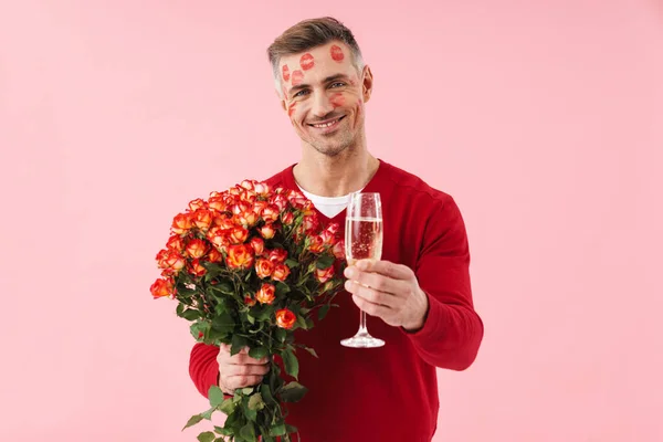 英俊的高加索男人的画像 脸上有亲吻的痕迹 手里拿着鲜花和香槟酒杯 背景是粉色的 — 图库照片