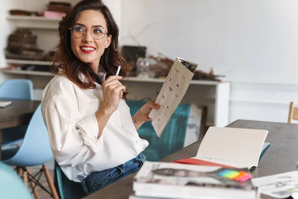 Vakker Smilende Ung Brunette Kvinne Som Leser Mens Hun Sitter – stockfoto