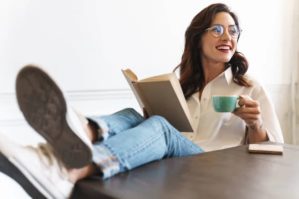 陽気若いですブルネット女性読書A本を読みながらリラックスホームでコーヒーのカップ — ストック写真
