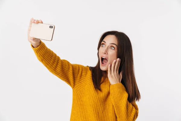 照片中美丽的黑发成年女性 身穿毛衣 面带微笑 在白色背景下的手机上自拍 — 图库照片