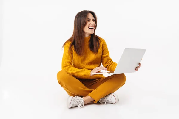美丽的黑发成年女性微笑着拿着手提电脑 双腿交叉坐在白色背景上的图片 — 图库照片