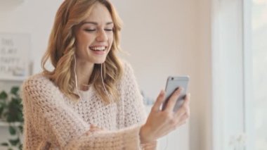 Gülümseyen mutlu bir kadın elini sallayarak beyaz bir kafede otururken bir video görüşmesi yapıyor.