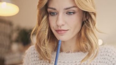 Ciddi düşünen genç bir sarışın kadın kapalı bir kafede bir şeyler yazıyor.