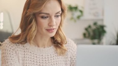 Çekici sarışın bir kadın bilgisayarını kapalı bir kafede kullanıyor.