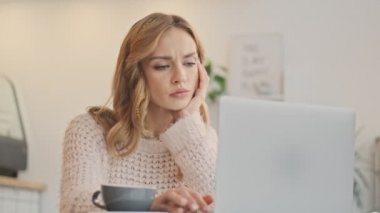 Ciddi şekilde hoşnutsuz genç bir kadın kapalı bir kafede dizüstü bilgisayarında daktilo yazıyor.