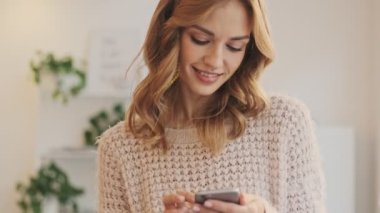 Odaklanmış bir kadın, kapalı bir kafede dururken akıllı telefonundan ilginç bir şey izliyor.