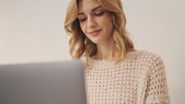一位积极乐观的年轻女性正与手提电脑一起工作 她孤零零地坐在室内白墙的背景下 — 图库视频影像