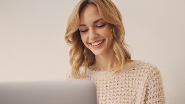 白い部屋で銀製のノートパソコンを操作している間に若い美しい女性が笑っています — ストック動画