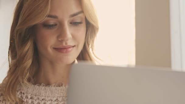 在阳光灿烂的日子里 一个快乐的微笑的年轻女人坐在白色舒适的咖啡店里 一边用她的银色笔记本电脑 — 图库视频影像