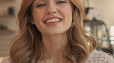 Kahkahalar atan genç bir kadının yakın çekim görüntüsü, rahat bir kafede otururken kameraya bakıyor.