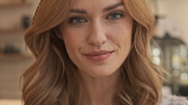 Sakin ve mutlu genç bir kadının yakın çekim görüntüsü, rahat bir kafede otururken kameraya bakıyor.