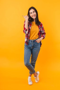 Neşe dolu genç bir kadının sarı arka planda parmakla işaret ettiği ve sırıttığı fotoğraf.